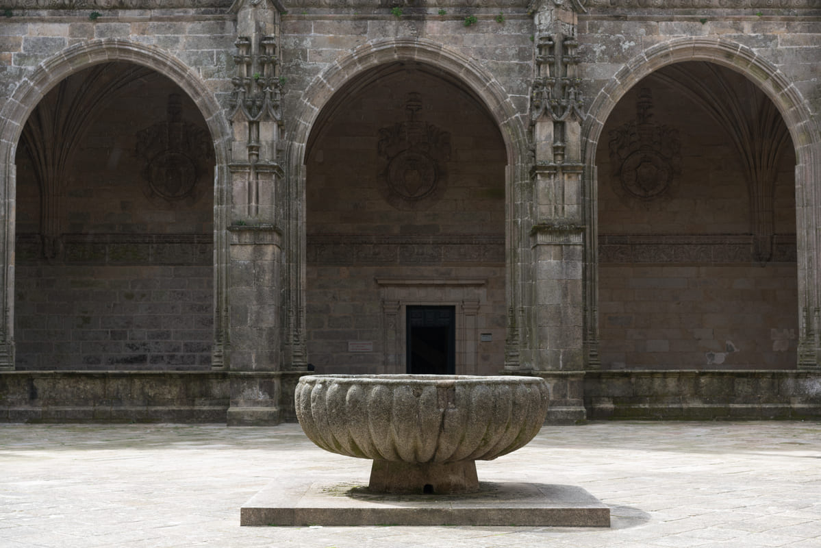 Vaso de granito gallonado de la Fons Mirabilis en el centro del claustro de la Catedral de Santiago, bajo las arcadas platerescas con escudos her&aacute;ldicos