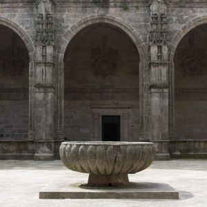 Vaso de granito gallonado de la Fons Mirabilis en el centro del claustro de la Catedral de Santiago, bajo las arcadas platerescas con escudos heráldicos