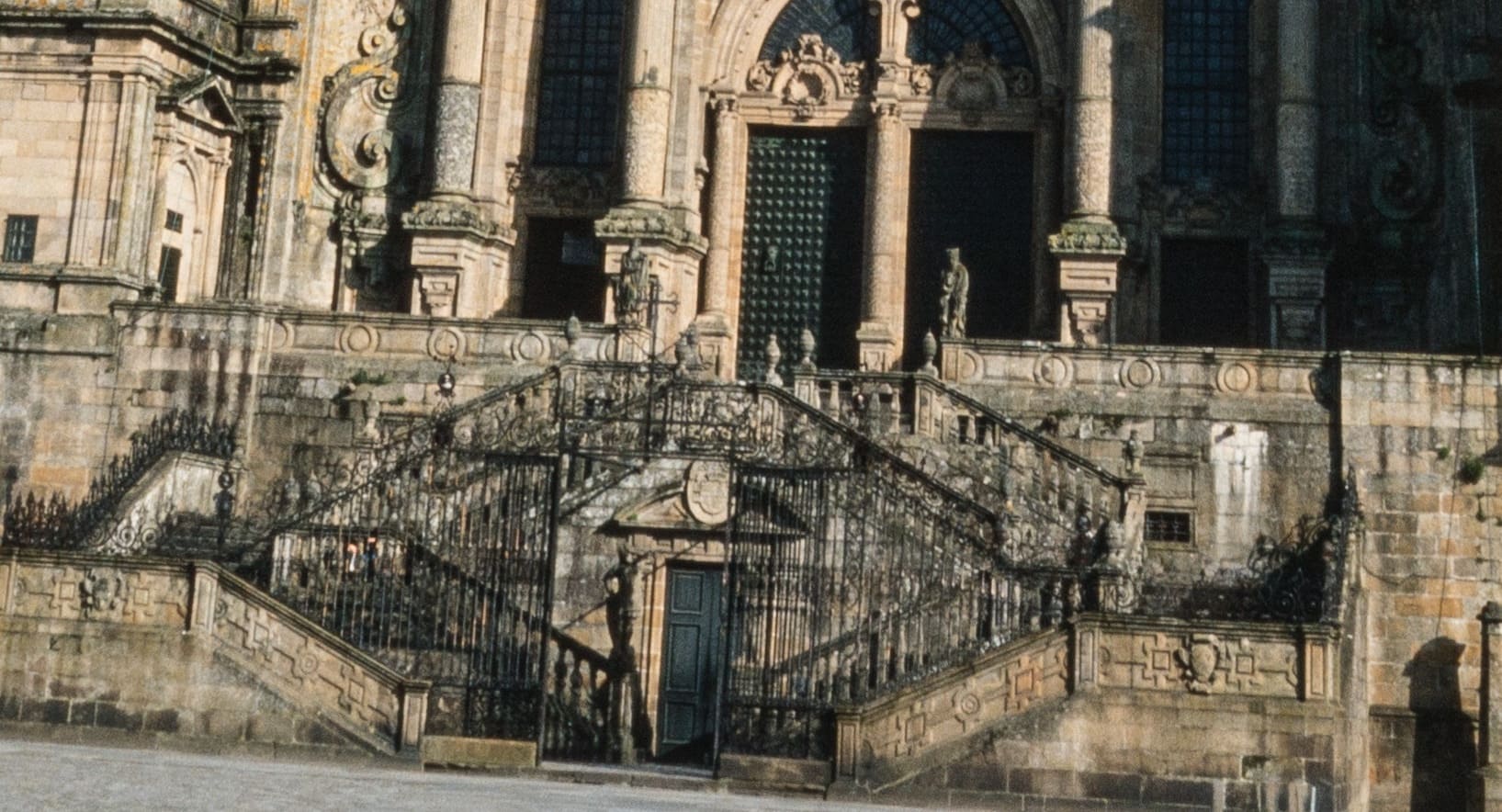 Doble escalinata en forma de rombo con barandillas de hierro forjado que asciende a la fachada del Obradoiro, con la puerta de la cripta rom&aacute;nica (Catedral Vieja) en el centro