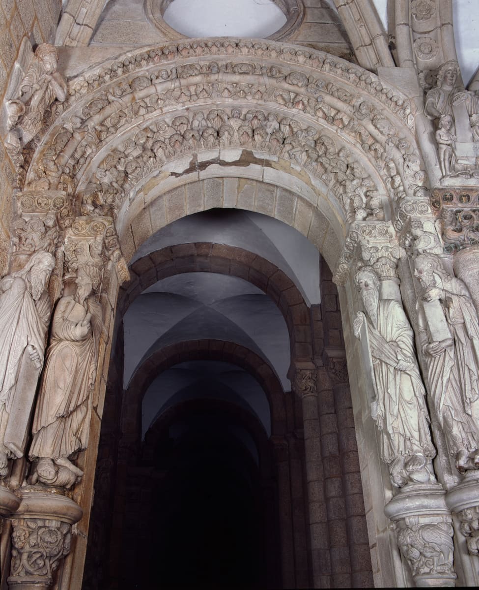 Arco lateral del P&oacute;rtico de la Gloria sin t&iacute;mpano, con las arquivoltas pobladas de figuras y un &oacute;culo de la b&oacute;veda del n&aacute;rtex sobre &eacute;l