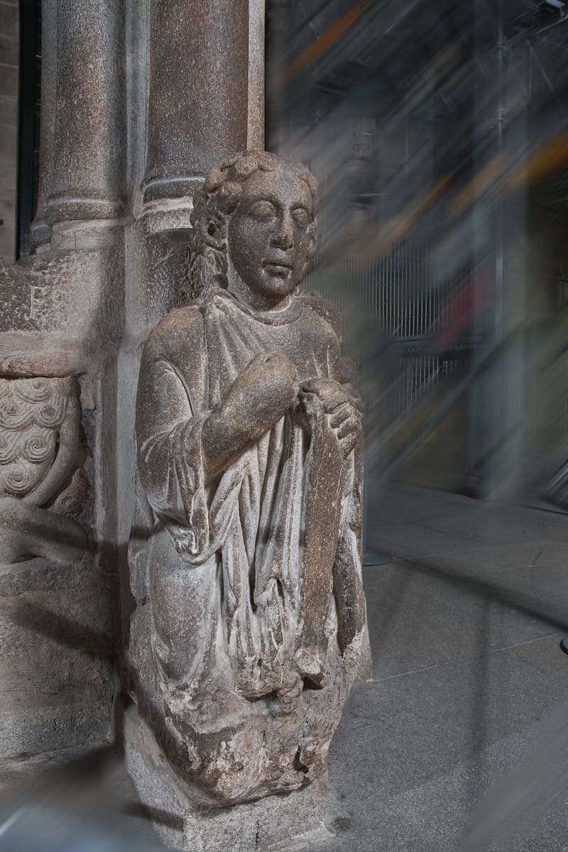 Figura arrodillada del Santo dos Croques en el P&oacute;rtico de la Gloria, considerada el autorretrato del Maestro Mateo, con el desgaste de siglos de cabezazos rituales de los estudiantes